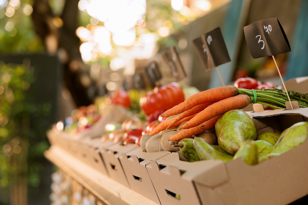 Closeup of vibrant freshly harvested organic produce at farmers market. Locally grown fruits and vegetables with price tags and bio products are available at the outdoor farm fair trade booth.